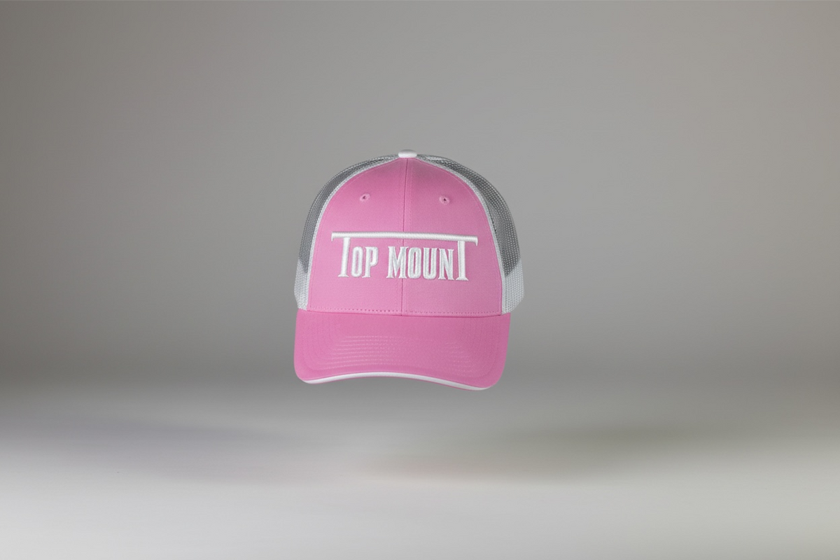 Women's pink Top Mount trucker hat with white embroidered logo, flat bill, and breathable mesh back.