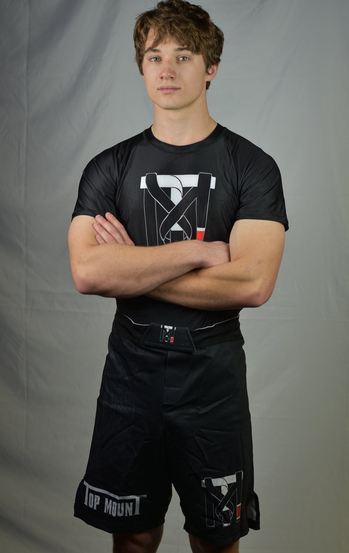 Youth athlete in a Top Mount Aztec BJJ rashguard and matching no-gi jiu jitsu shorts with arms crossed.