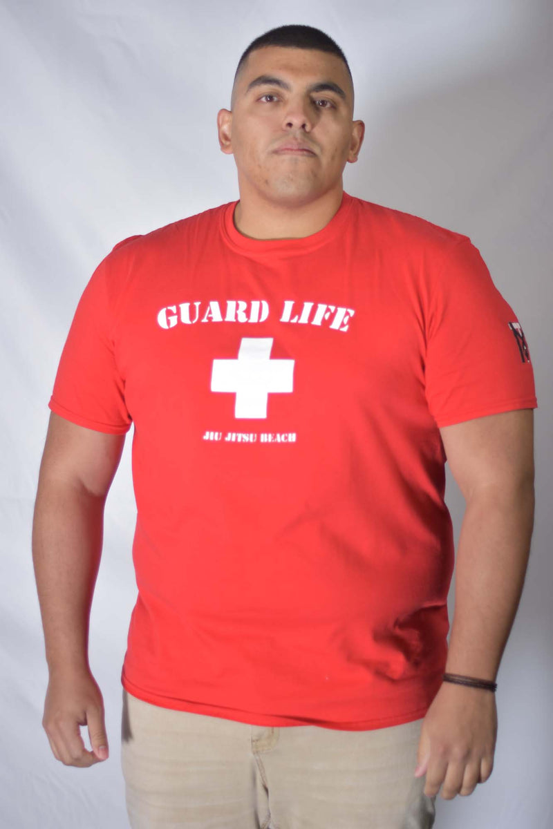 Man wearing red Guard Life Jiu Jitsu Beach Tee with white cross logo and Top Mount BJJ sleeve branding.