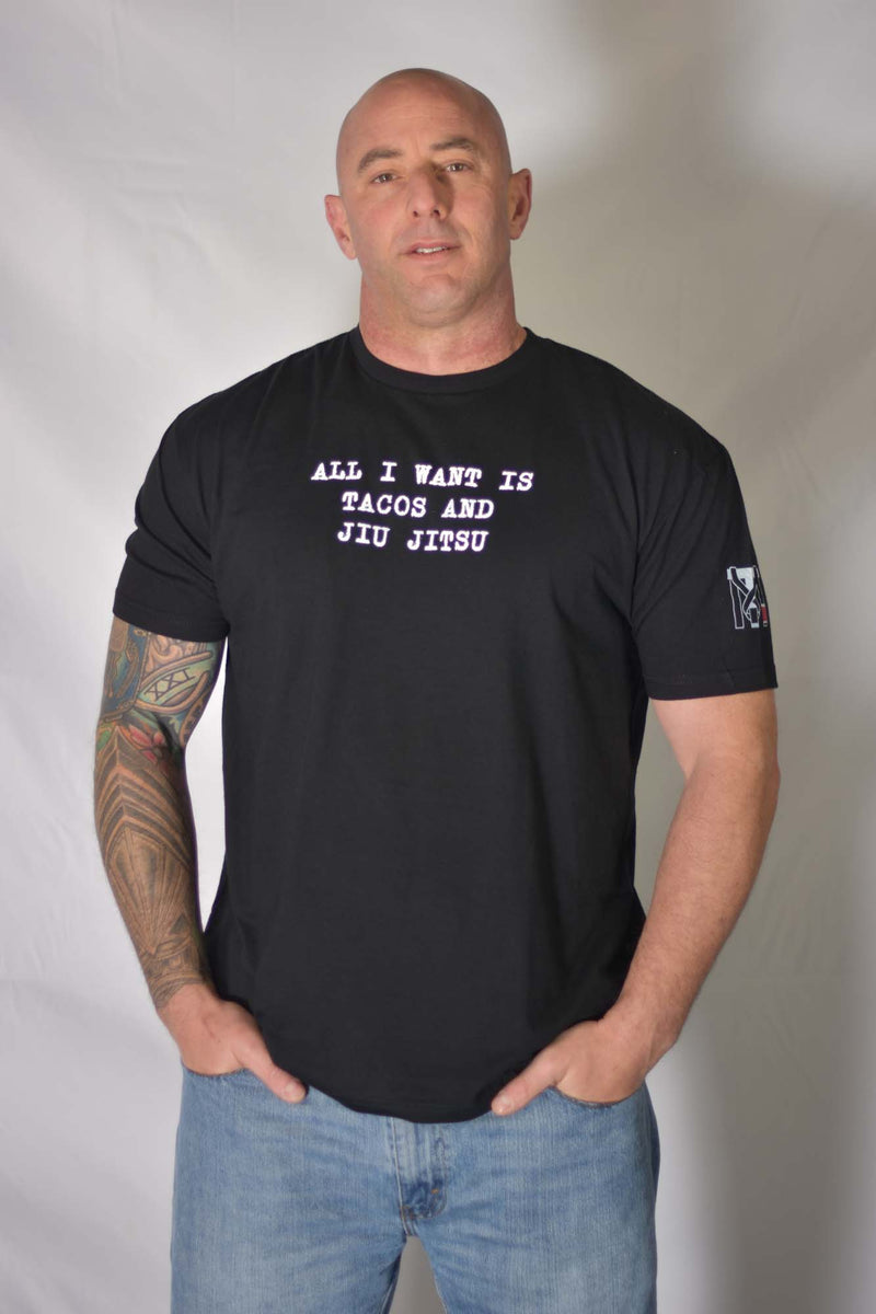 Man in Top Mount BJJ Tacos Graphic Tee with 'All I Want Is Tacos And Jiu Jitsu' text and sleeve logo detail.