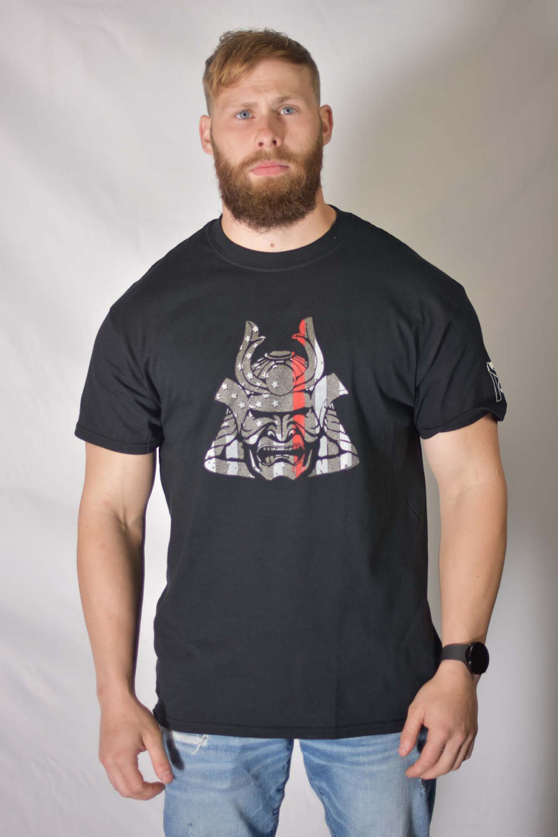 Man in Firefighter Samurai T-Shirt featuring a red line warrior helmet graphic with American flag details on black cotton.