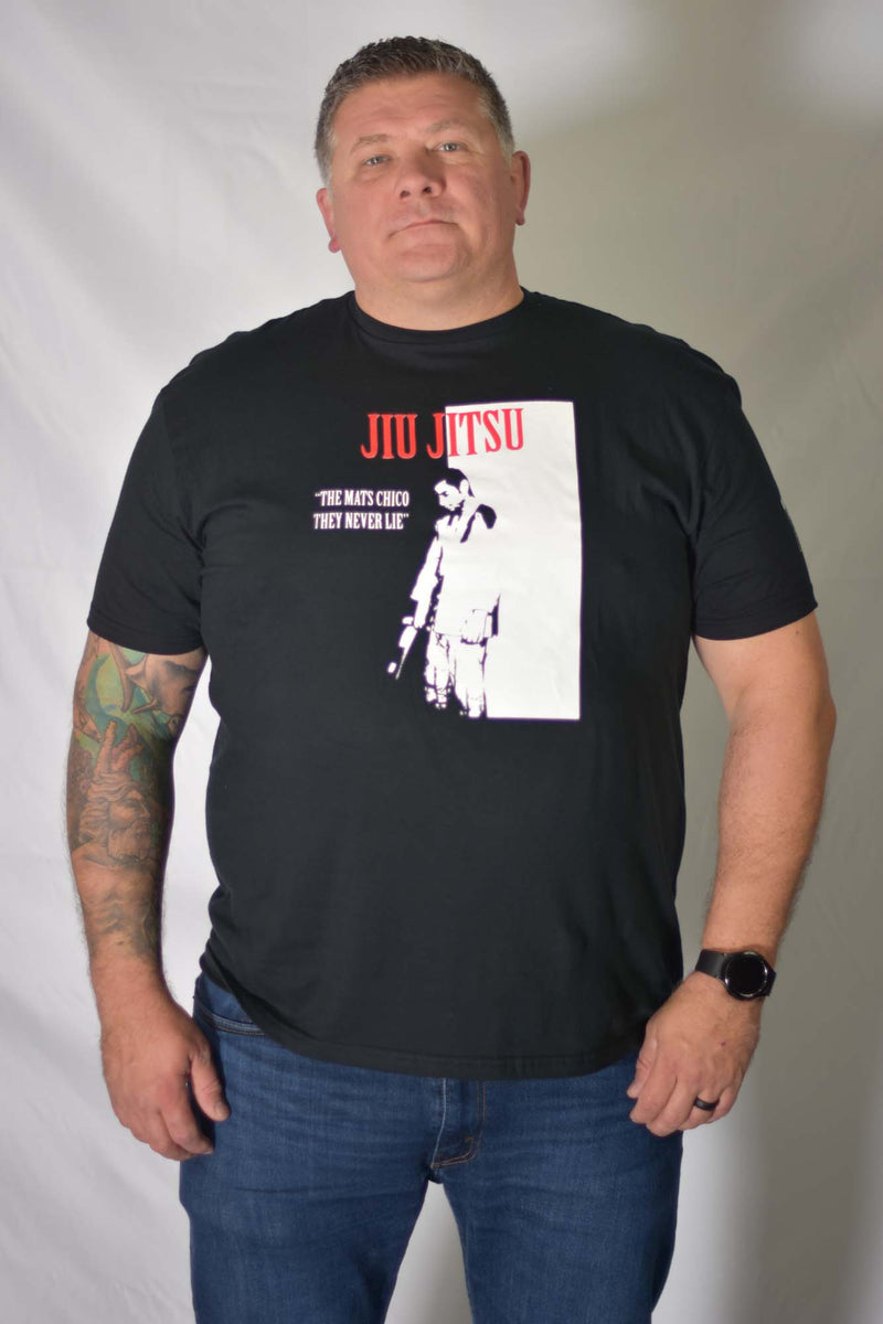 Man wearing a black BJJ Scarface Graphic Tee with 'The Mats Chico They Never Lie' and Jiu Jitsu movie-style print.
